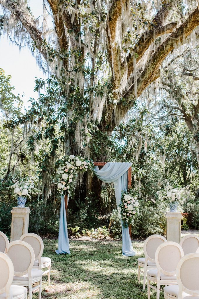 Beautiful wedding ceremony with a wooden arbor, light blue chiffon draping, and amazing a symmetrical floral arrangements at Magnolia Plantation and Gardens