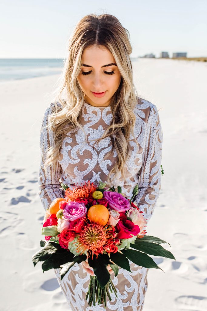 Bride holding a tropical theme wedding bouquet with bright pink, green, purple florals, and real florida oranges made by Destin florist, Destin Floral Designs.