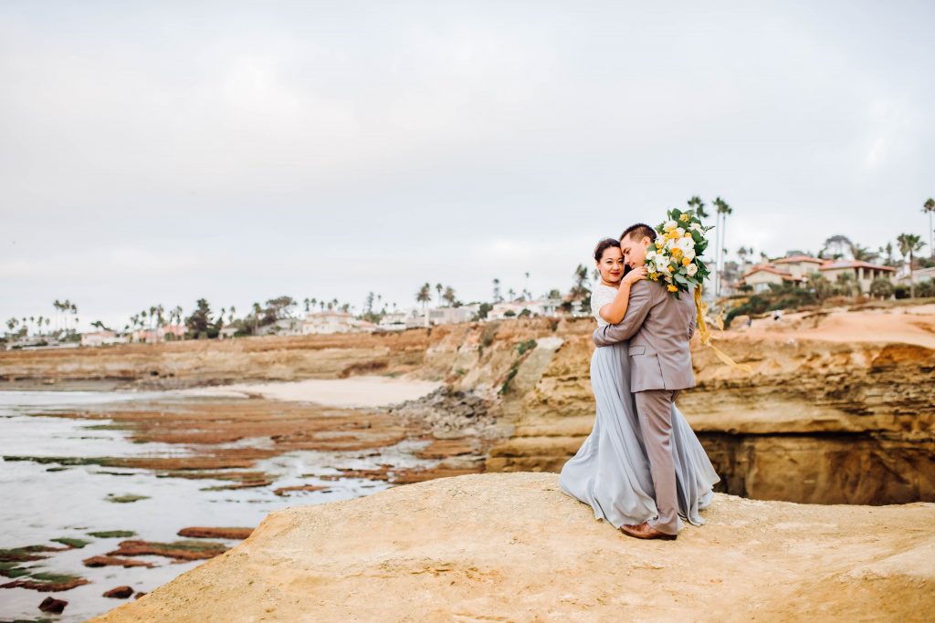 Bride and groom embracing on the edge of sunset cliffs in San Diego, CA